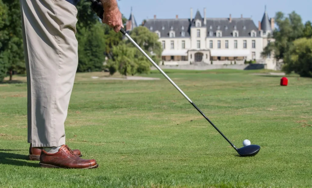 Image qui illustre l'activité du Golf au Château GOLF & SPA d'Augerville, un homme s'apprête à tirer sa balle de golf, avec le Château en fond