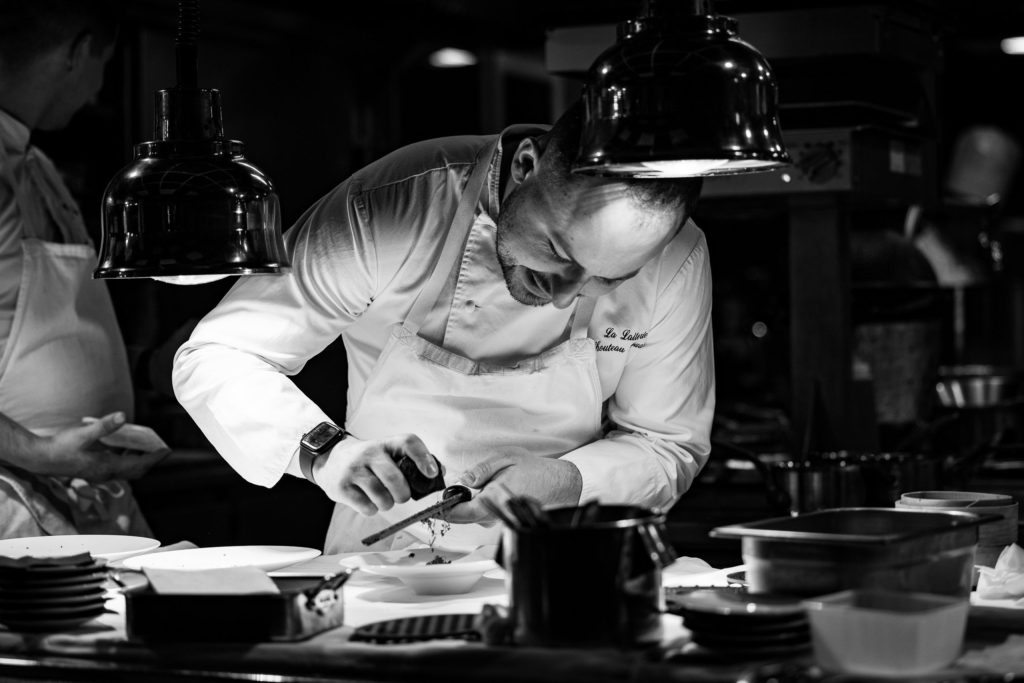 Photographie en noir et blanc du Chef cuisinier Edouard Chouteau e train de cuisiner, souriant et concentré