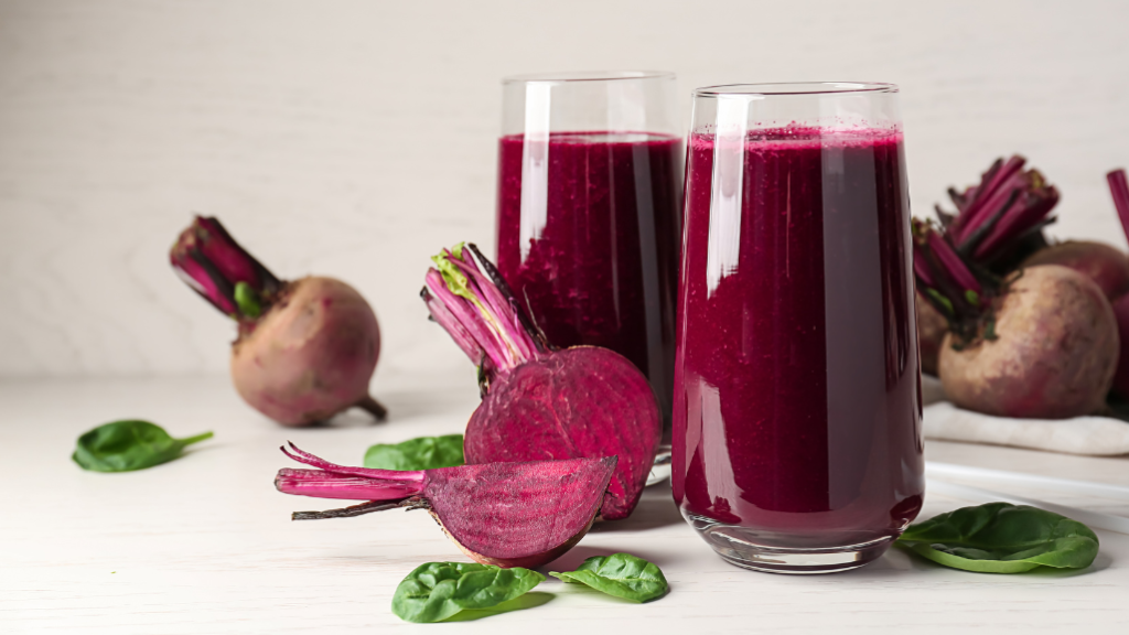 Due bicchieri di smoothie alla barbabietola su sfondo bianco, con barbabietole sparse intorno